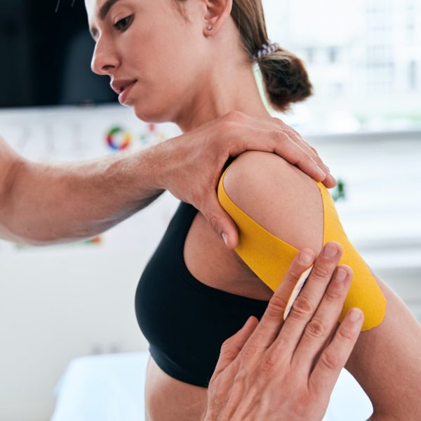 Unrecognized manual therapist taping yellow tape on patient shoulder in wellness center